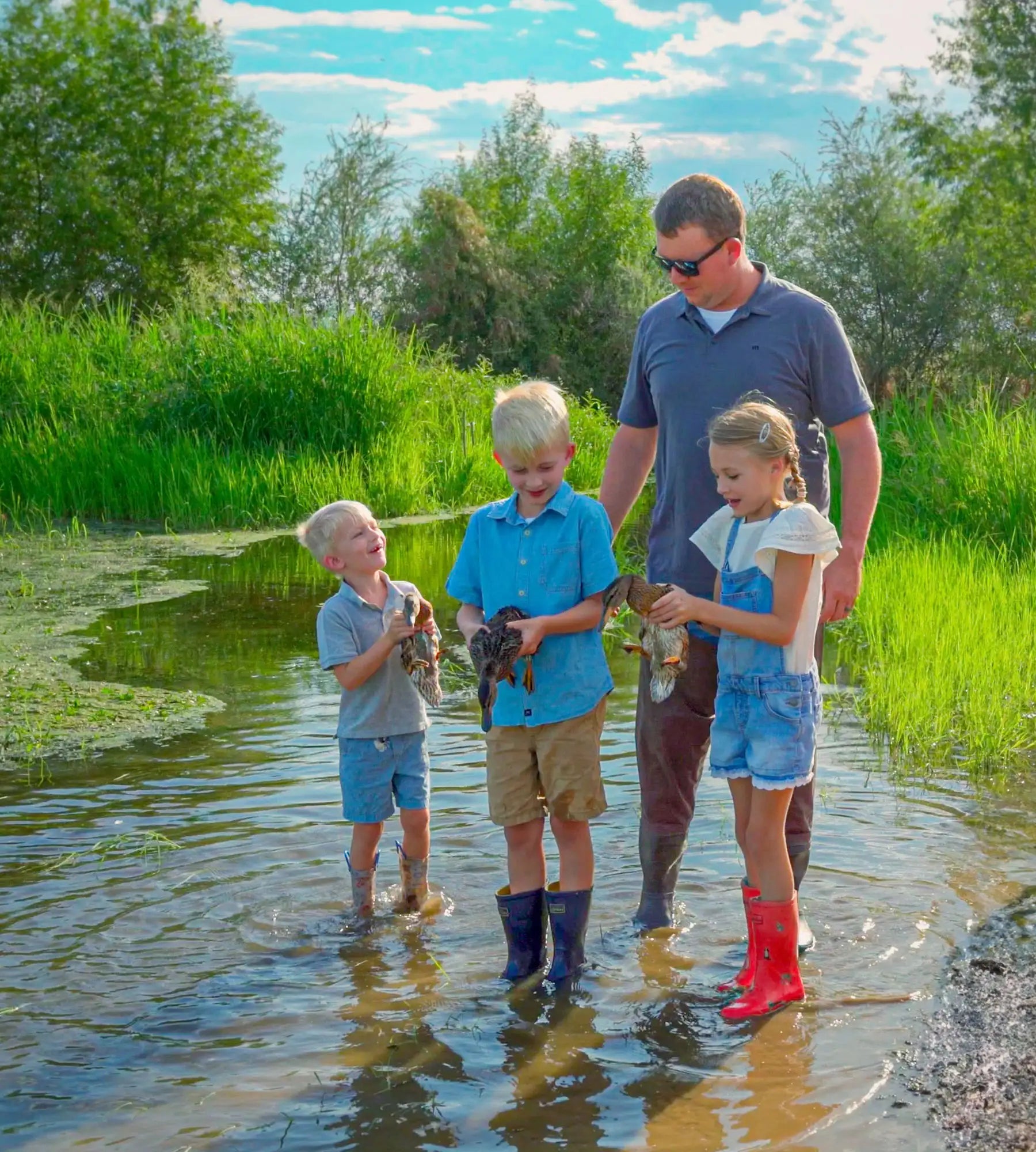 Man with three children in shallow water with waders on holding ducks